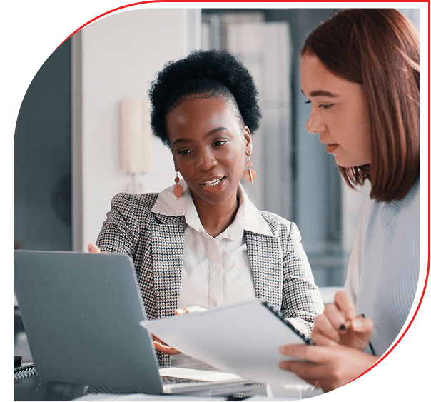 Two women collaborating over documents and a laptop.