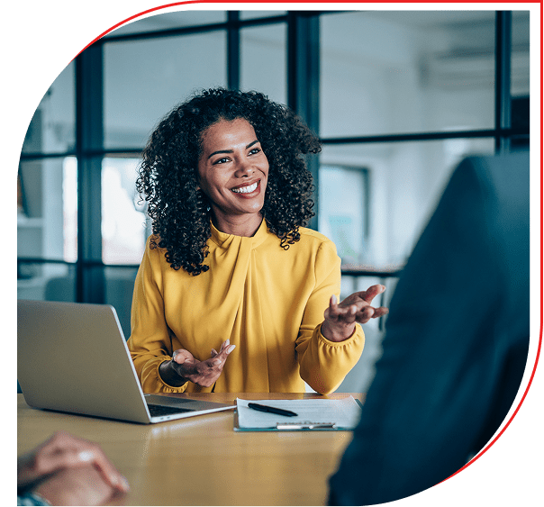 A woman in a yellow sweater smiling and talking during a meeting.
